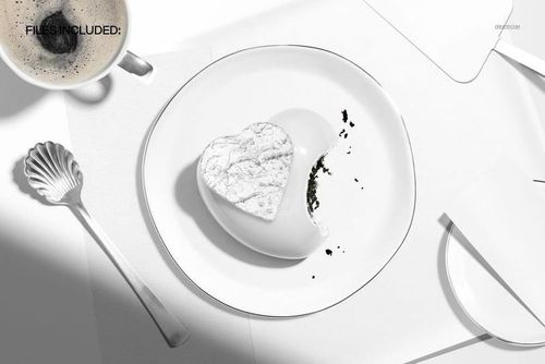 Heart shaped mousse cake with a bite taken out, placed on a white plate next to a cup of coffee and a shell-shaped spoon.