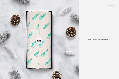 Gift box mockup featuring white tissue paper with teal lettering, surrounded by pinecones and frosted branches, top view.