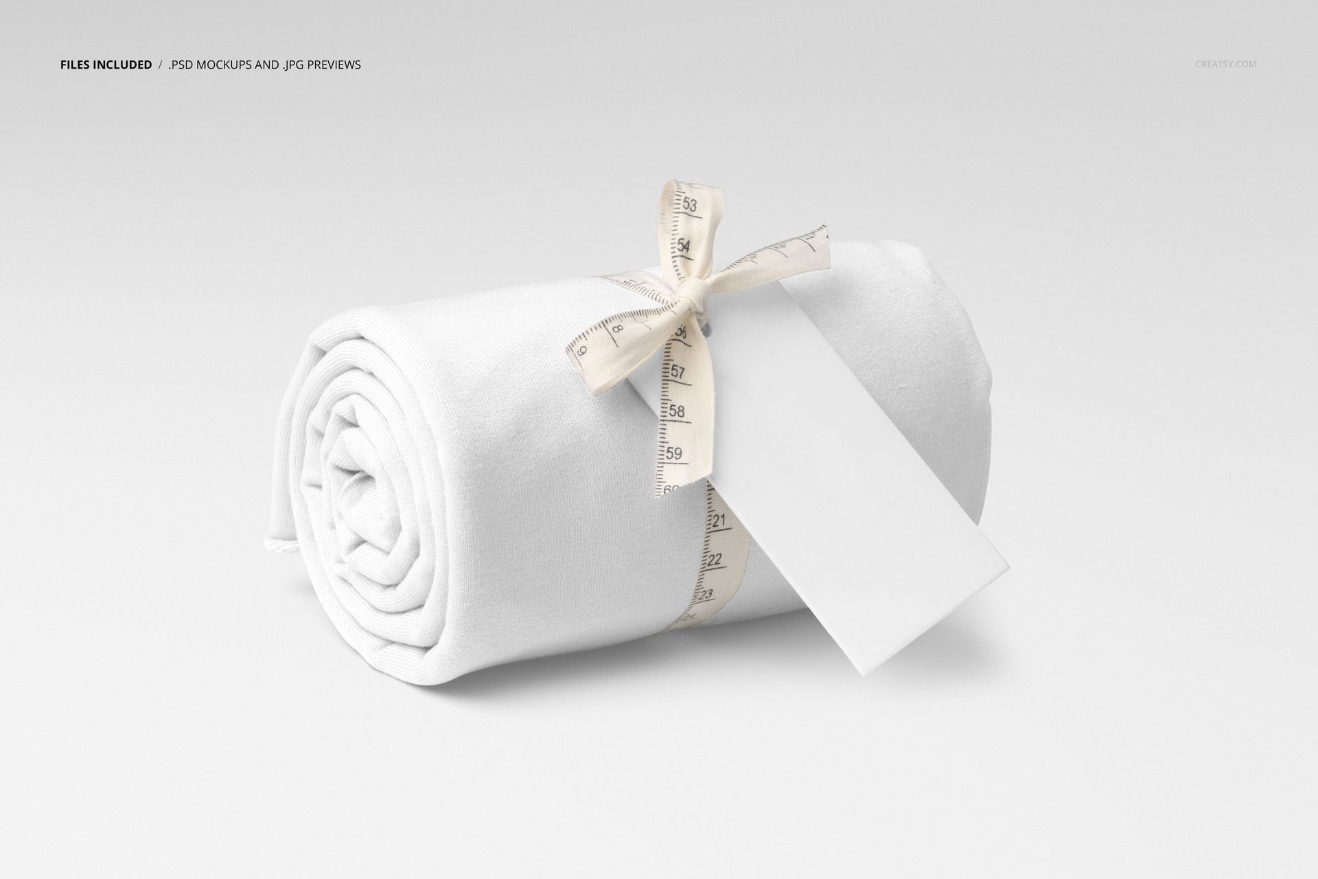 PSD mockup showing a rolled white fabric with a bow made of measuring tape and a blank tag on a neutral background.