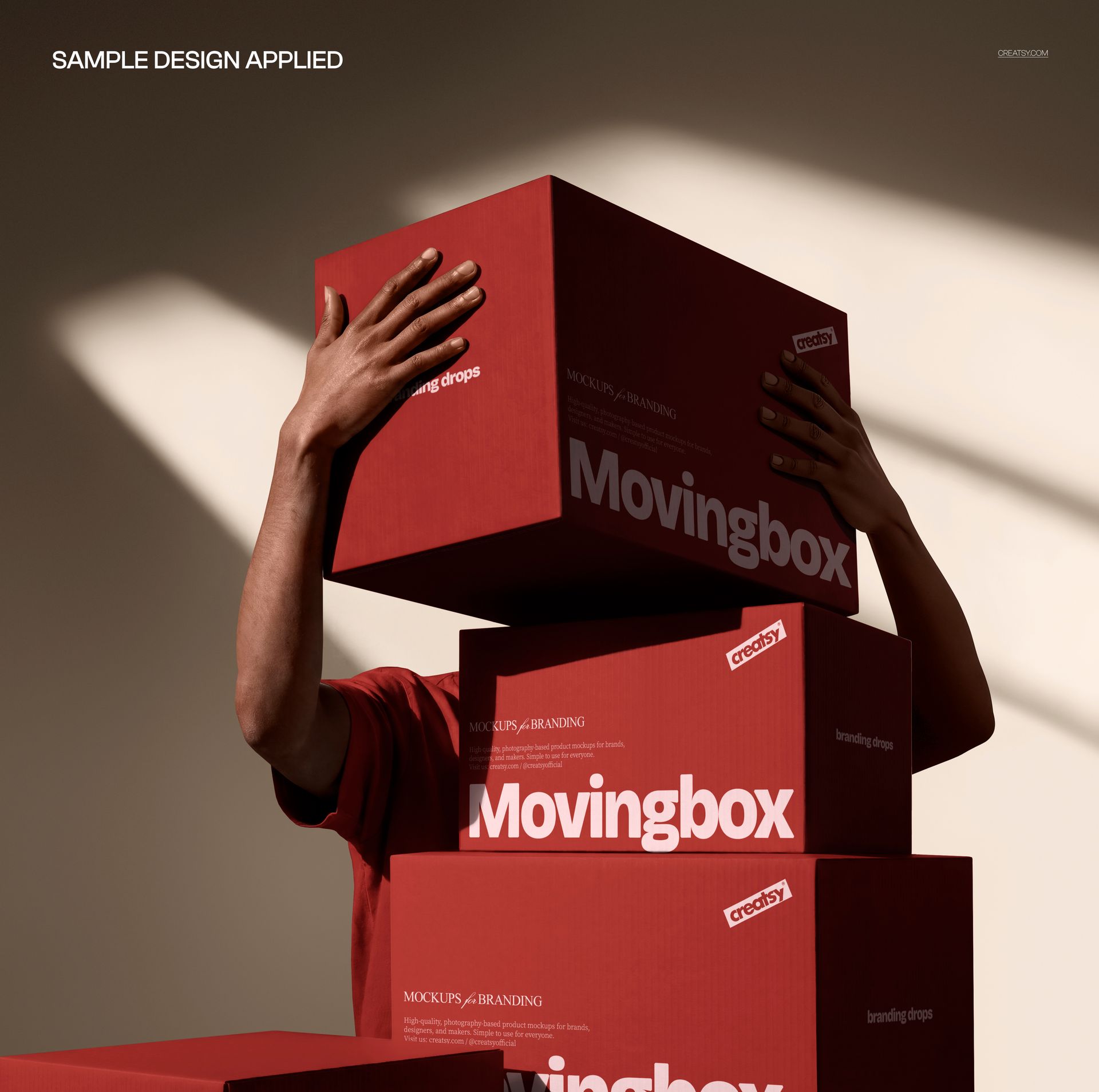 Front view of a person partially hidden behind three red packaging boxes mockup stacked vertically in a sunlit room.