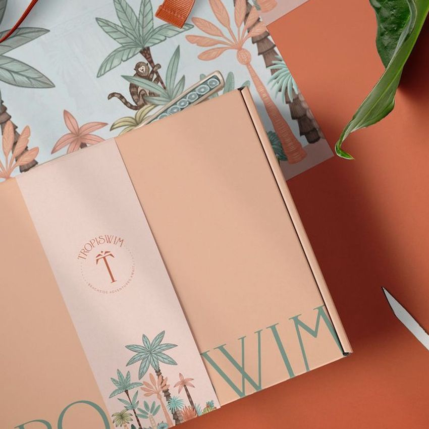 Packaging mockup featuring a peach-colored mailing box with tropical leaf illustrations and green text, set on a warm orange surface.