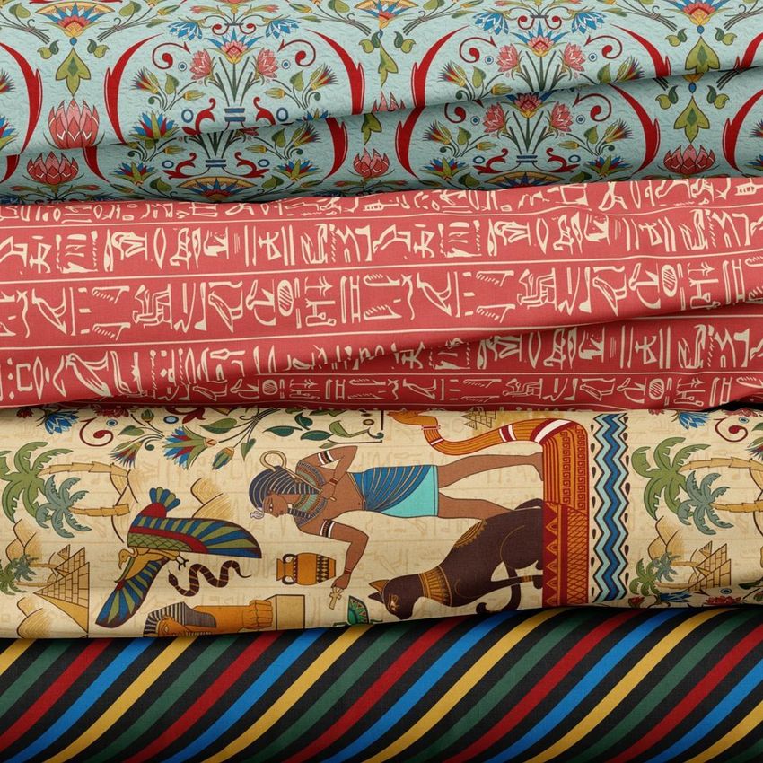 Fabric stack mockup showing four folded textiles with ancient Egyptian motifs, including hieroglyphs and colorful patterns.