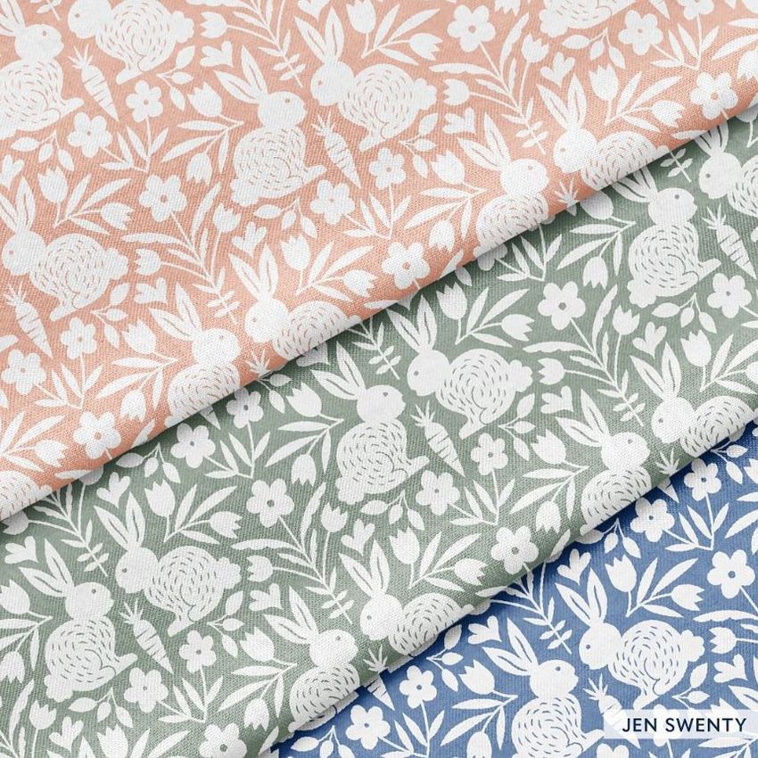 Cotton fabric mockup featuring three folded pieces with a white bunny and floral pattern in peach, green, and blue colors.