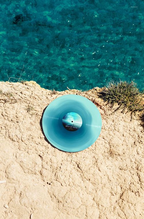 Colored vinyl record mockup shown from above on a textured rocky surface near vibrant blue sea water.