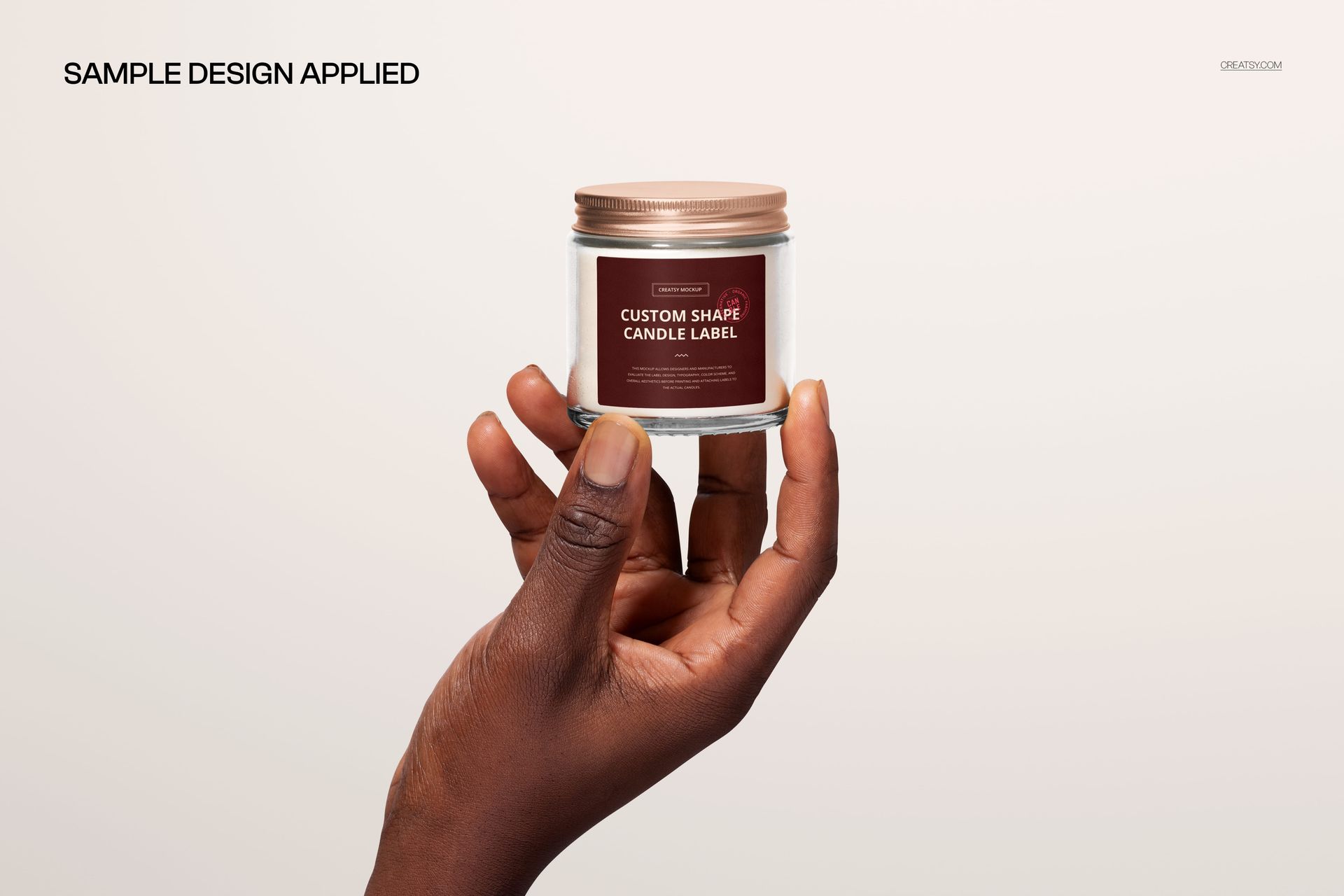 Clear glass candle jar with metallic lid held in a hand, featuring a custom label mockup on a light background.