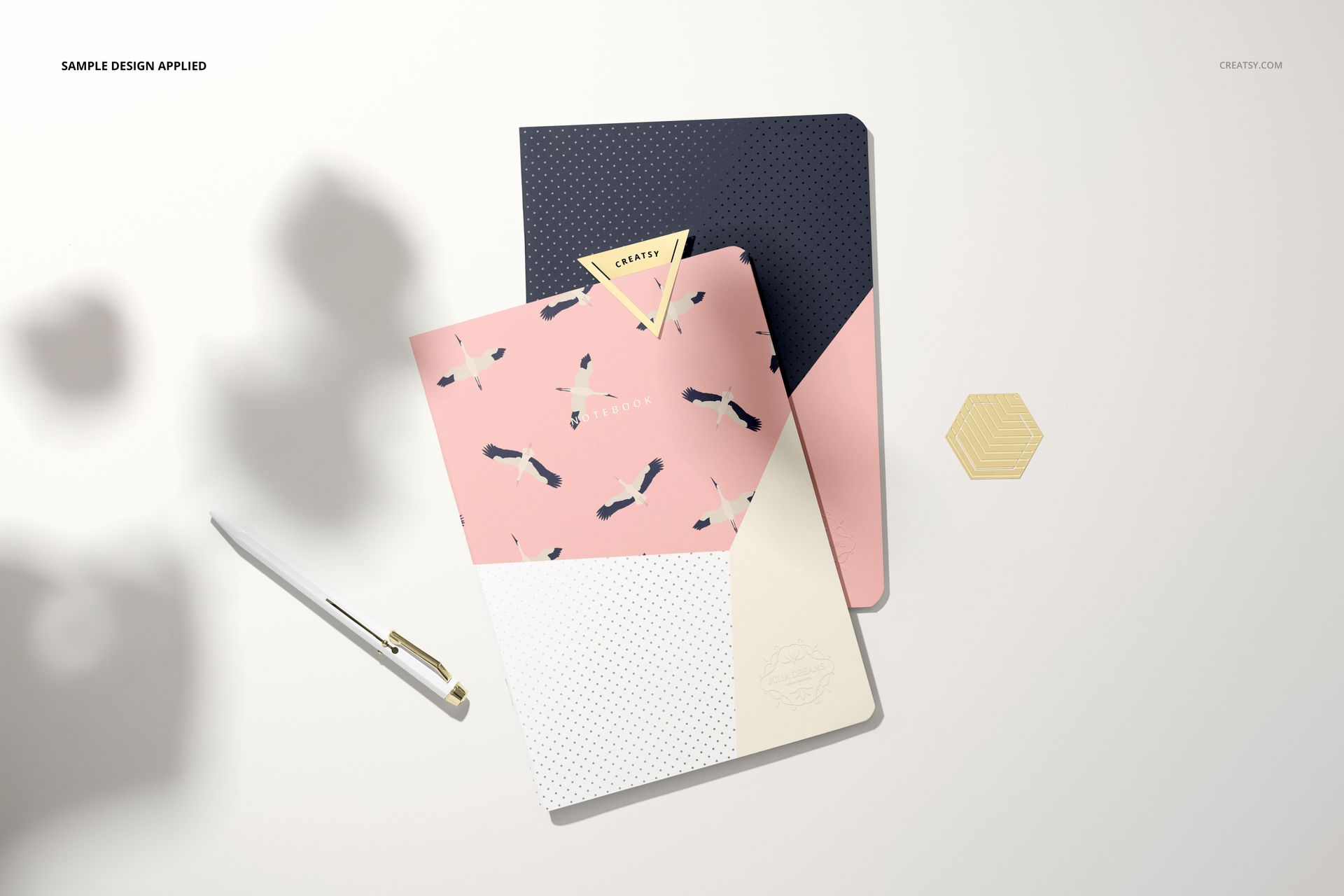 Notebook mockup set featuring two closed notebooks with abstract geometric designs, pen, and hexagonal prop.