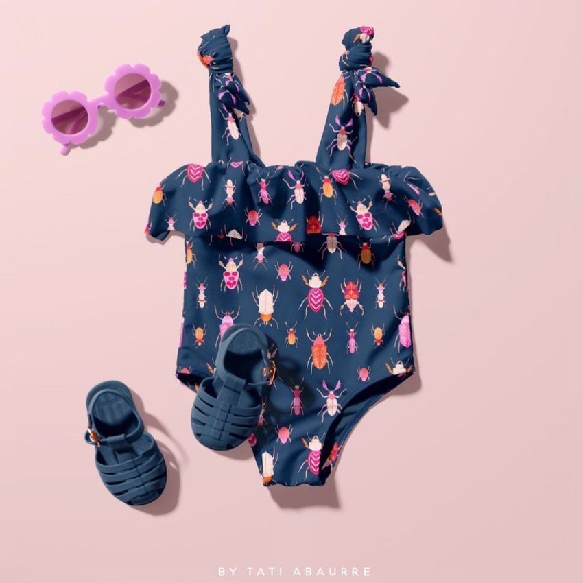 Baby swimsuit mockup with colorful beetle pattern, styled with blue sandals and pink flower-shaped sunglasses on a pastel background.