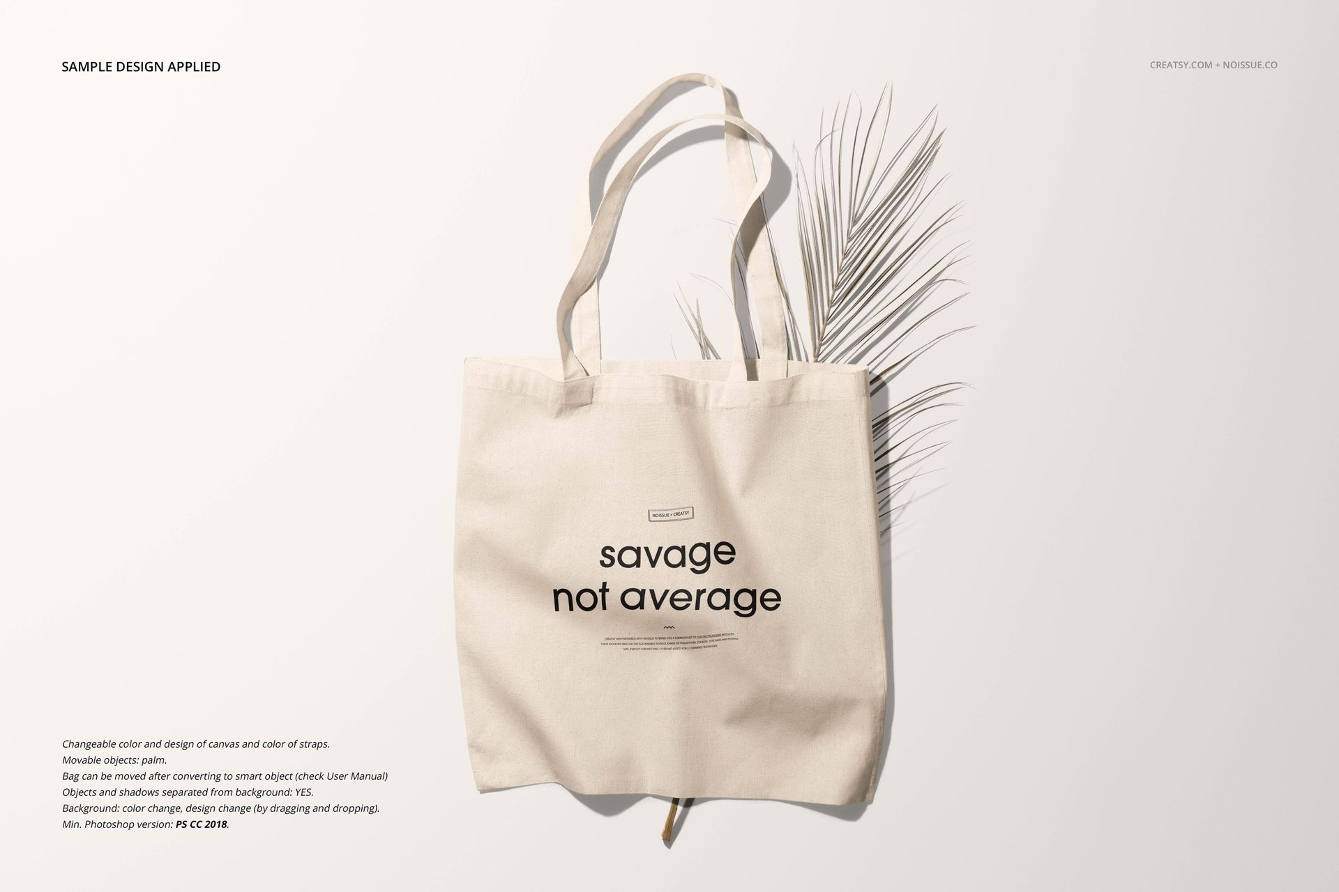 Front view of a beige tote bag mockup with printed text, displayed on a light surface with a dried palm leaf.