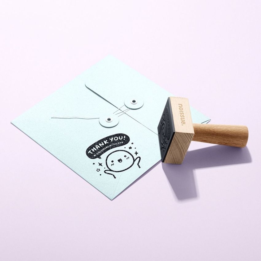 Wooden stamp mockup set on a pastel surface, featuring a stamped envelope with a cartoon character and thank you message.