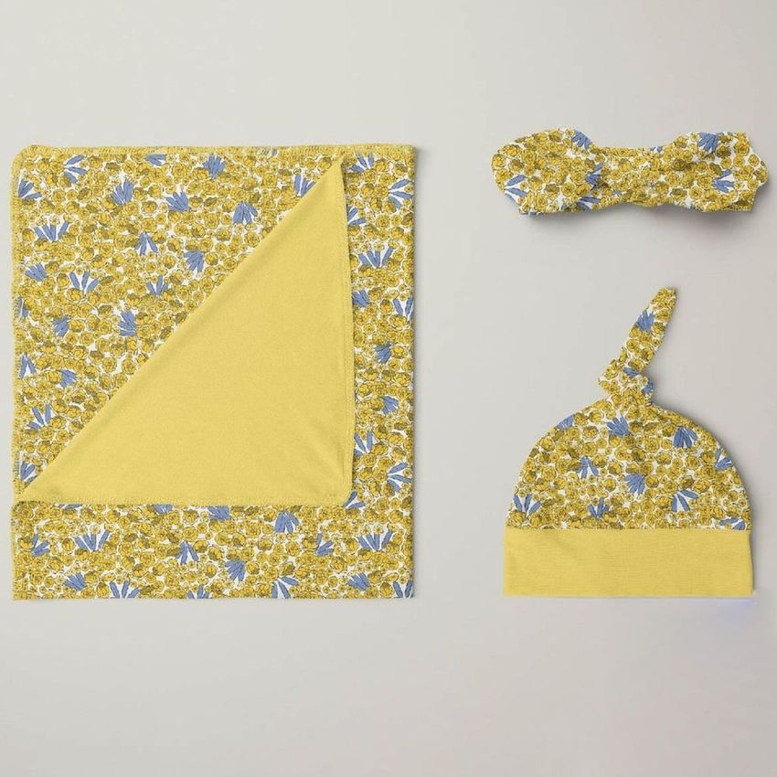 Swaddle set mockup featuring a yellow blanket, knotted hat, and bow headband with blue and white floral patterns on a neutral background.
