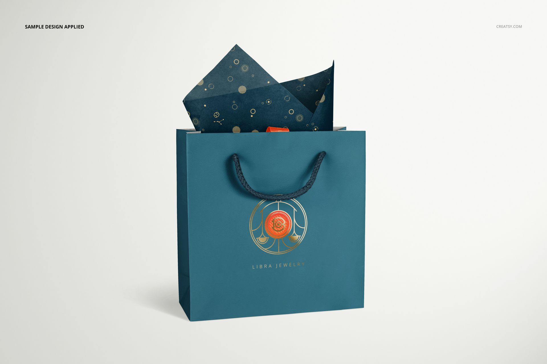 PSD mockup showing a teal jewelry gift bag with a decorative emblem and dark tissue paper with circular motifs peeking out.
