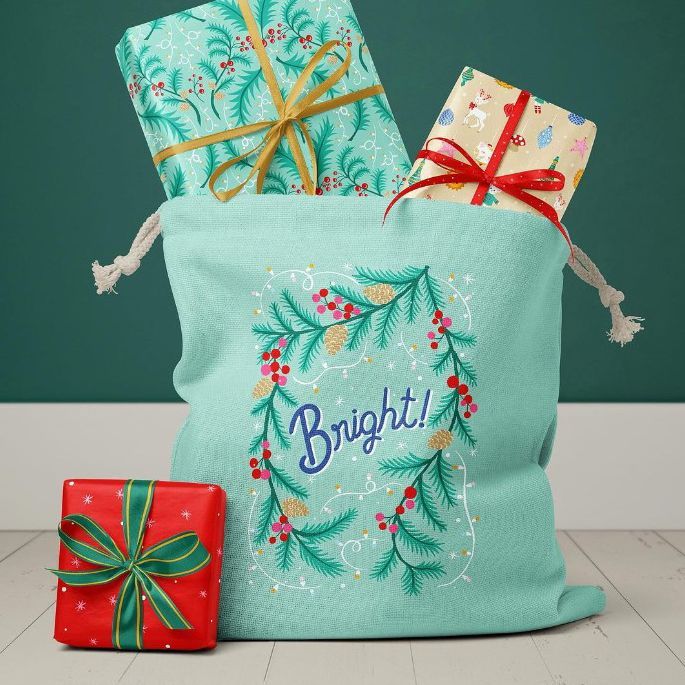 Santa bag mockup featuring a light blue fabric bag with festive pine and berry design, filled with three wrapped presents.