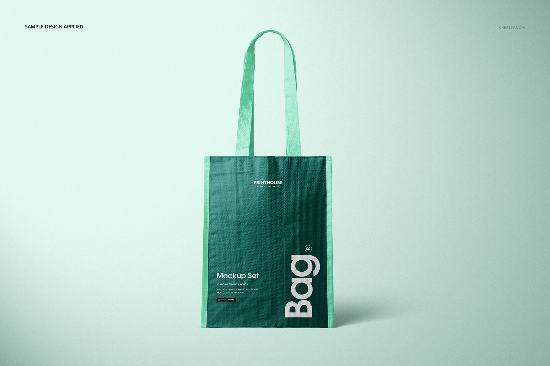 Woven tote bag mockup shown upright with green color, long straps, and minimalist text, set on a pale surface.