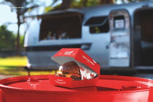 Open burger box mockup on a red barrel, showing a burger and paper liner, with a shiny food truck behind.