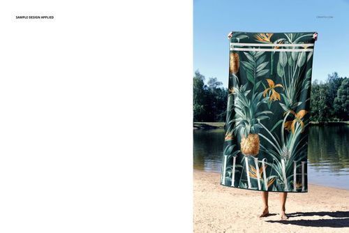 Front view of a beach towel mockup featuring a green botanical design, displayed outdoors by a lake.