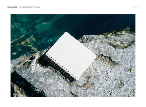 Blank spiral-bound planner lying on textured rocks near turquoise water, shown from above in a PSD mockup scene.
