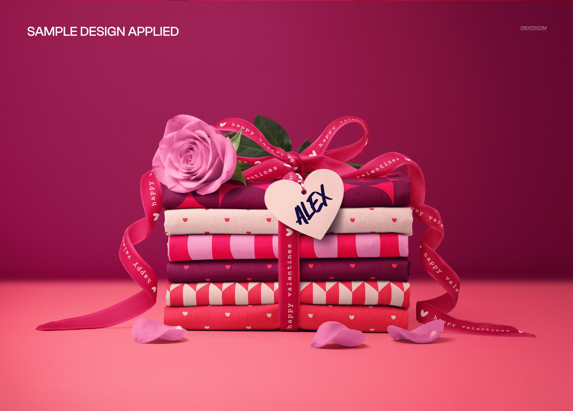 Fabric stack mockup featuring various pink and red patterns, velvet ribbon, rose, and heart tag, front view.