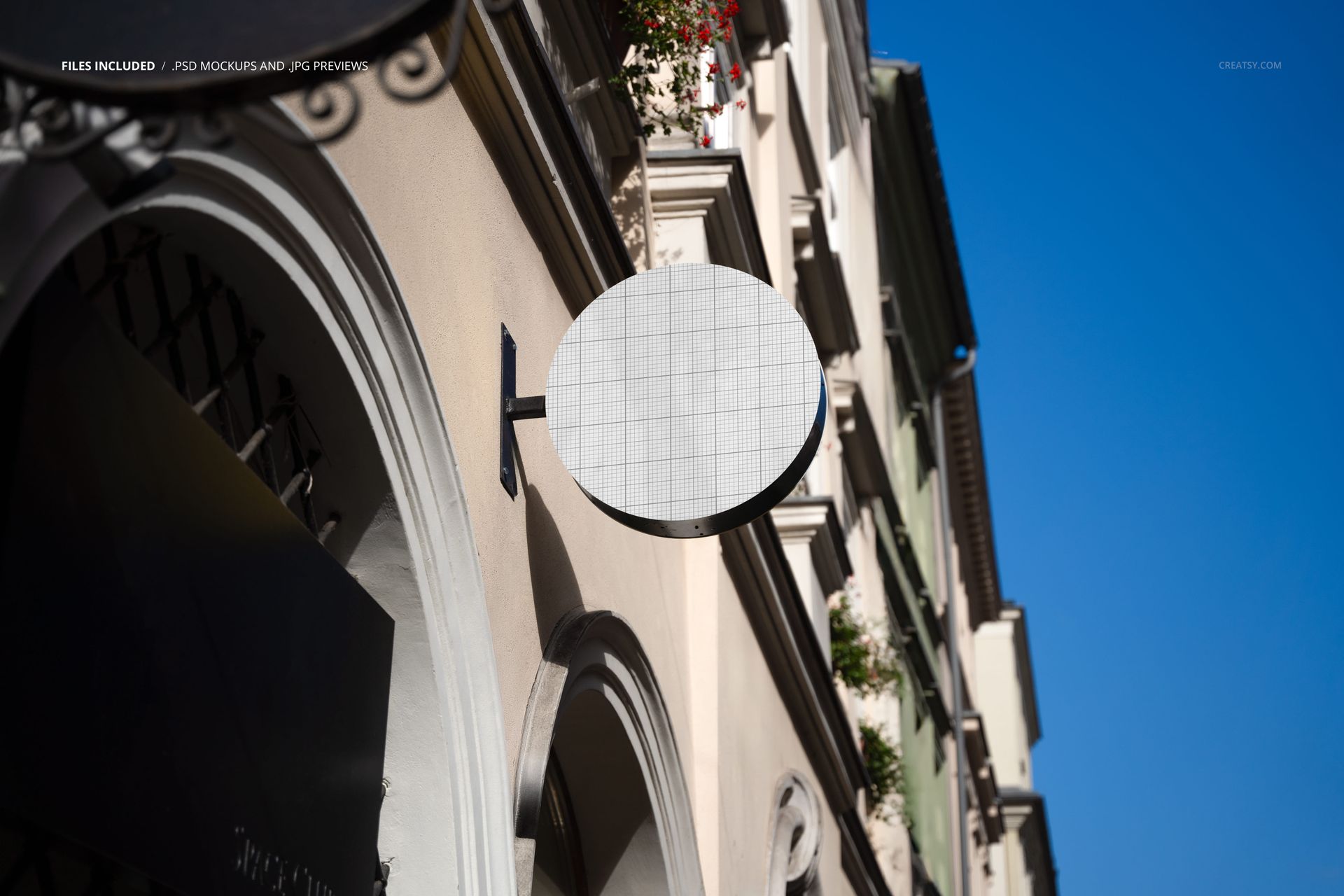 Round signboard mockup mounted on a building facade in an old town street, shown from a low angle perspective.