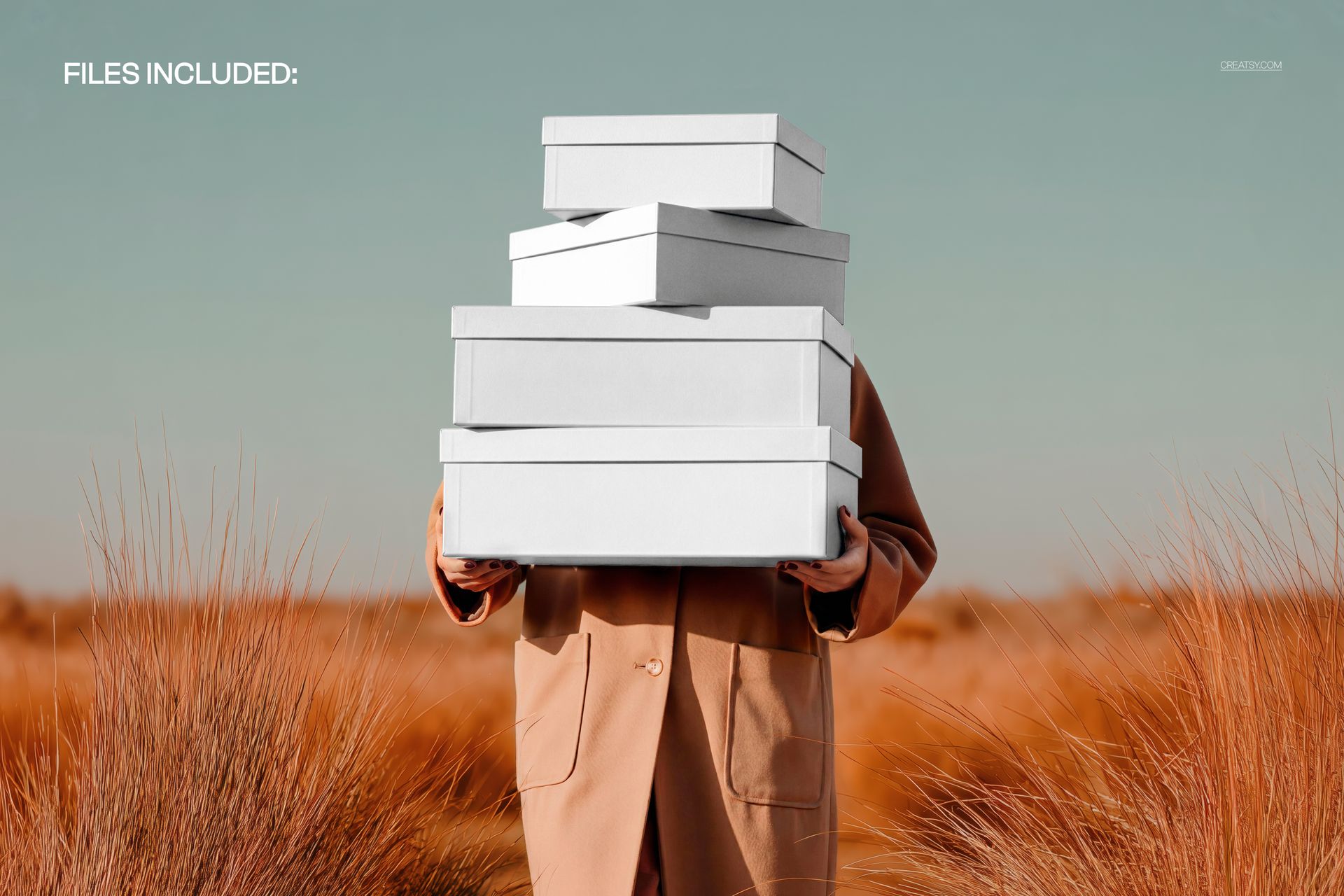Front view of a woman in a tan coat holding a stack of white shoe boxes in a pampas grass field mockup scene.