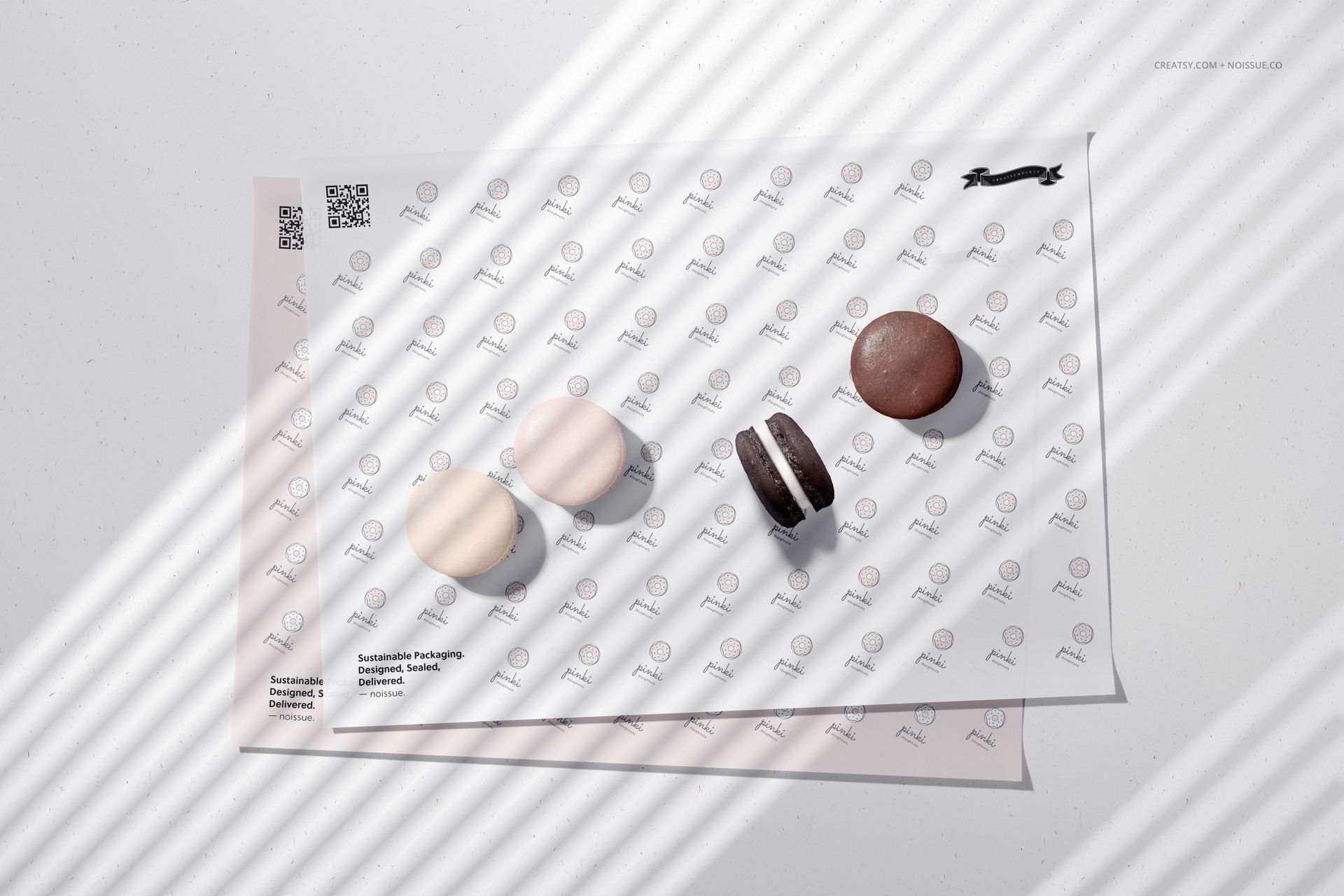 PSD mockup showing food safe paper with repeating logo design, holding pastel and chocolate macarons under soft light.