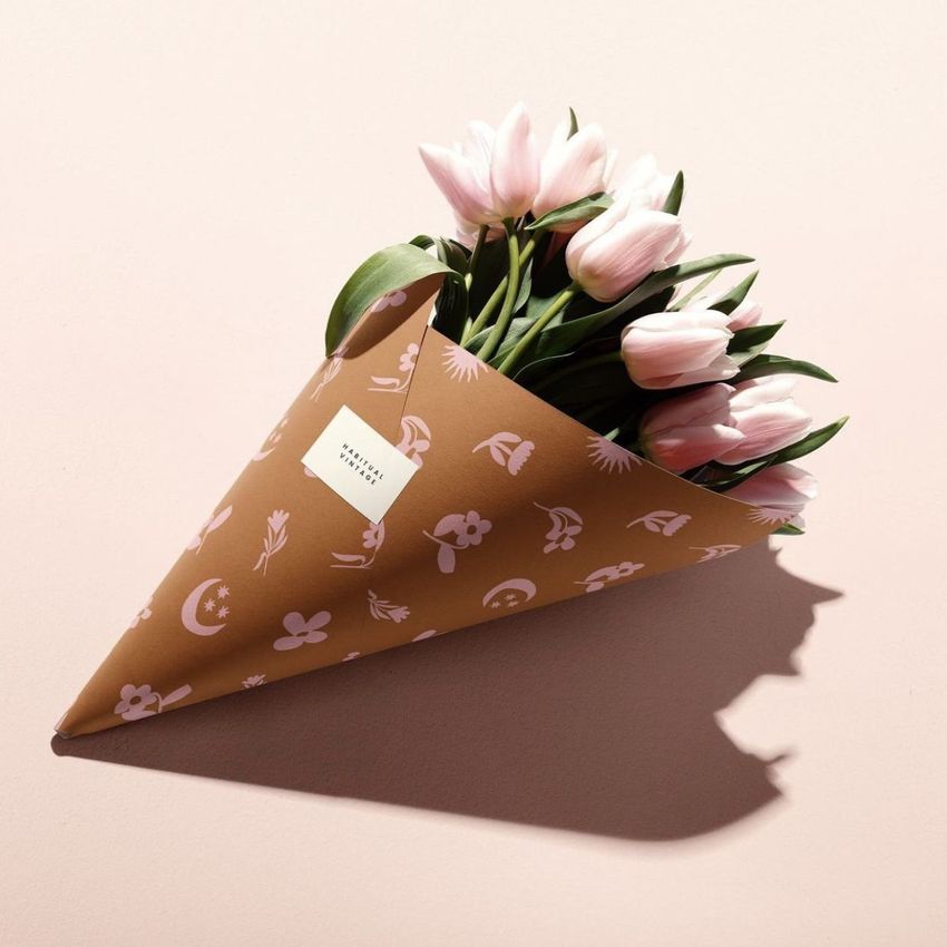 Sticker mockup featuring a bouquet of pink tulips wrapped in brown paper with white floral graphics and a square sticker label.