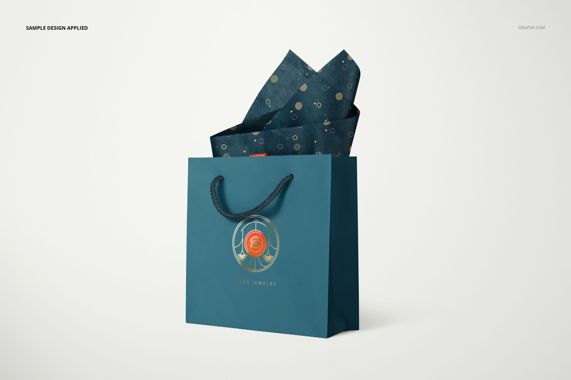 Jewelry box mockup scene featuring a blue gift bag with a circular gold emblem and patterned tissue paper protruding.