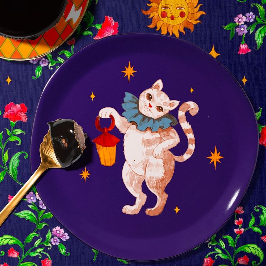 Plate mockup featuring a whimsical cat illustration holding a lantern, set on a dark purple plate with star accents.