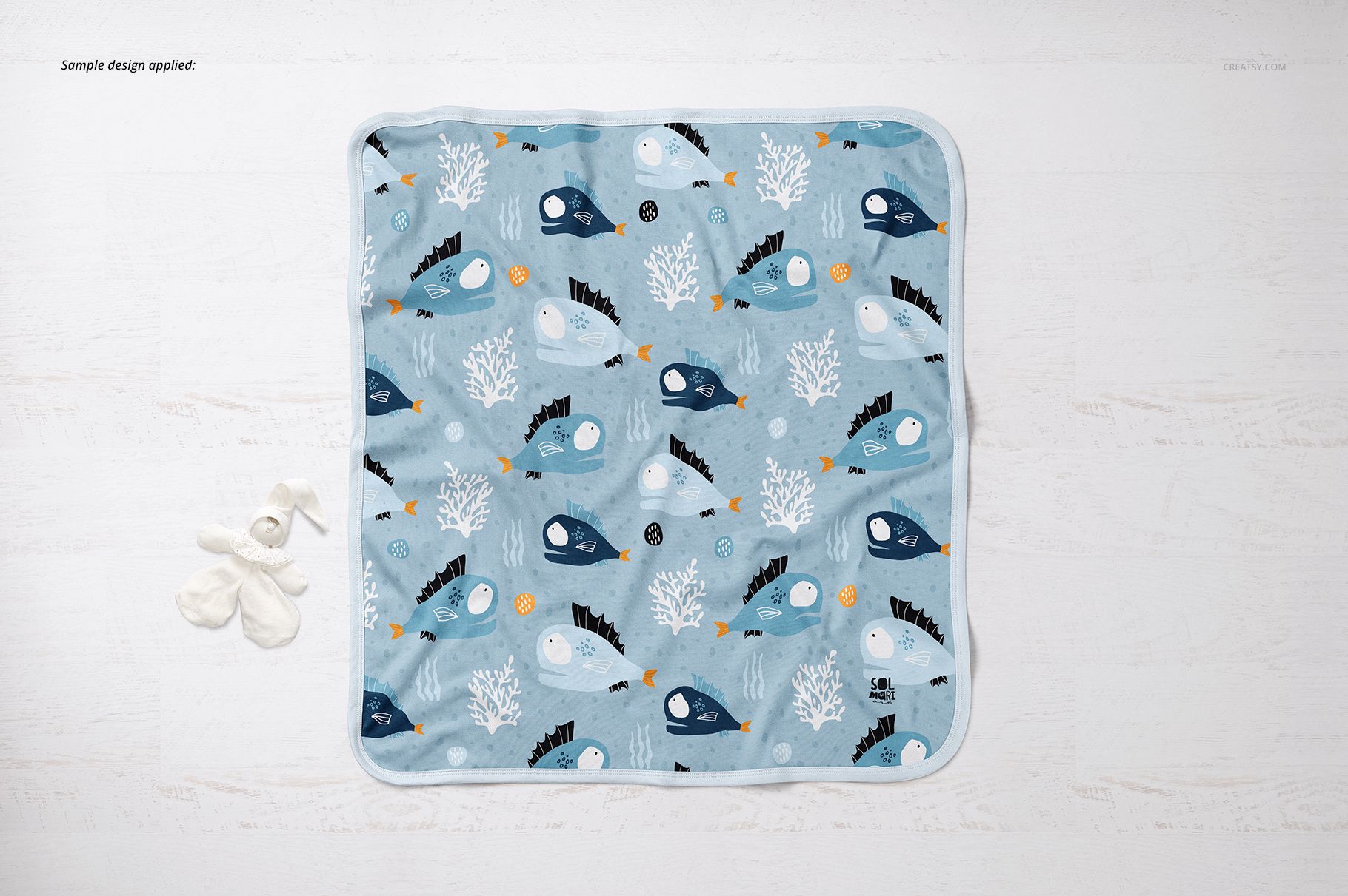 Blue cotton baby blanket mockup with fish and coral illustrations, shown from a top view on a light background.