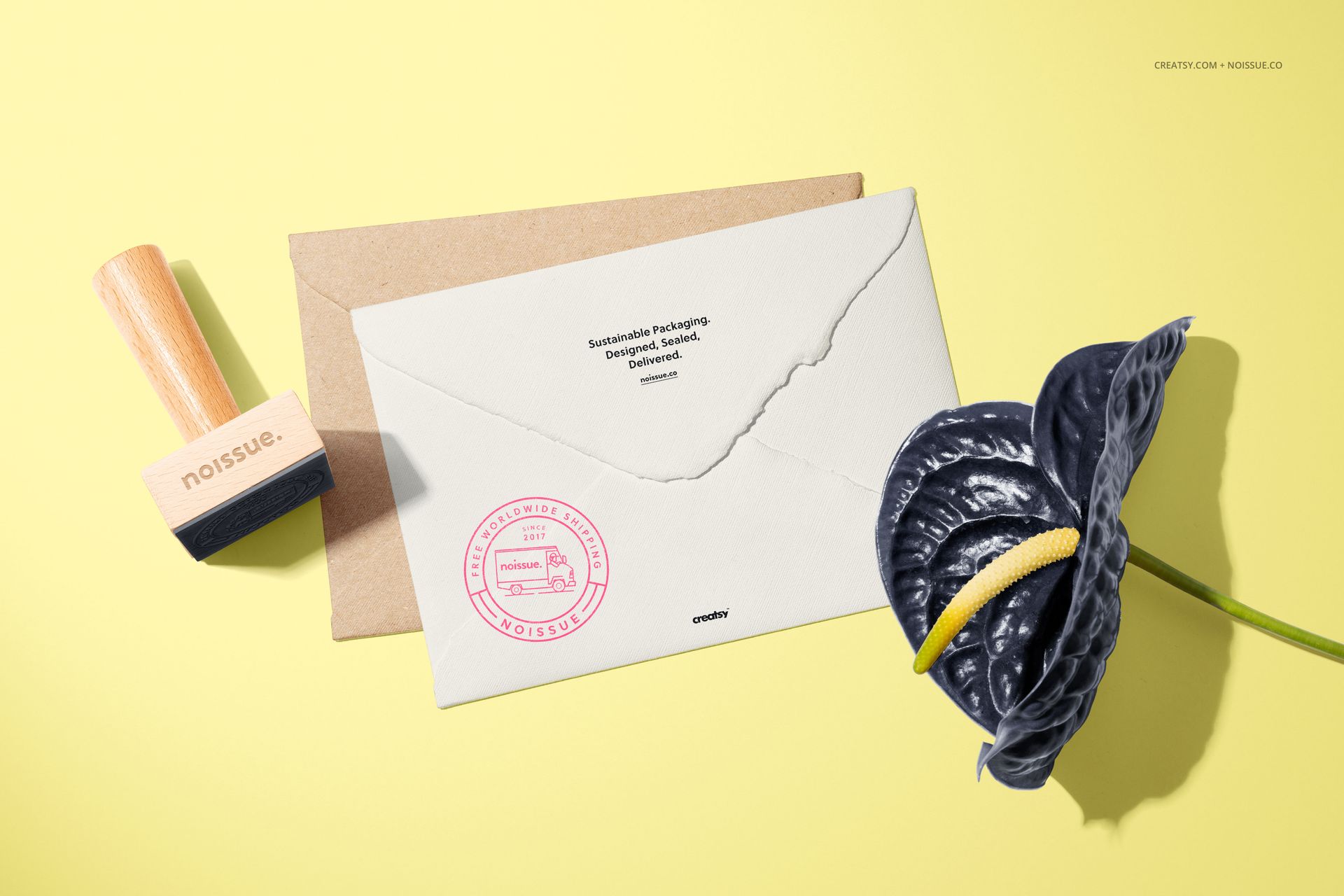 Stationery mockup featuring a wooden stamp, white envelope with stamped design, kraft card, and black flower.