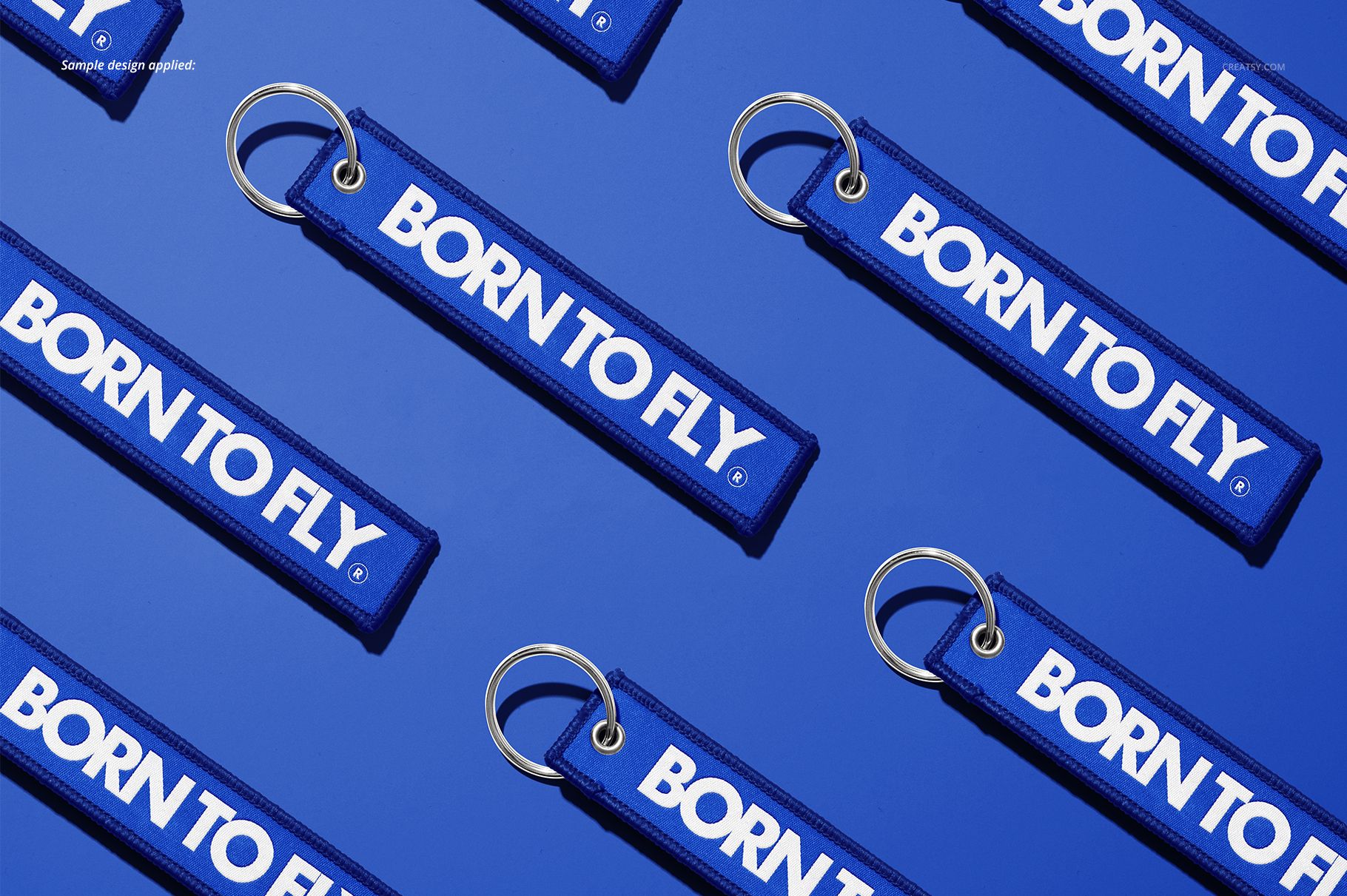 PSD mockup showing blue fabric keychains with silver rings and white text, laid out in a repeating pattern on a blue surface.