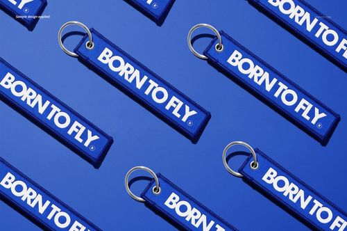 PSD mockup showing blue fabric keychains with silver rings and white text, laid out in a repeating pattern on a blue surface.