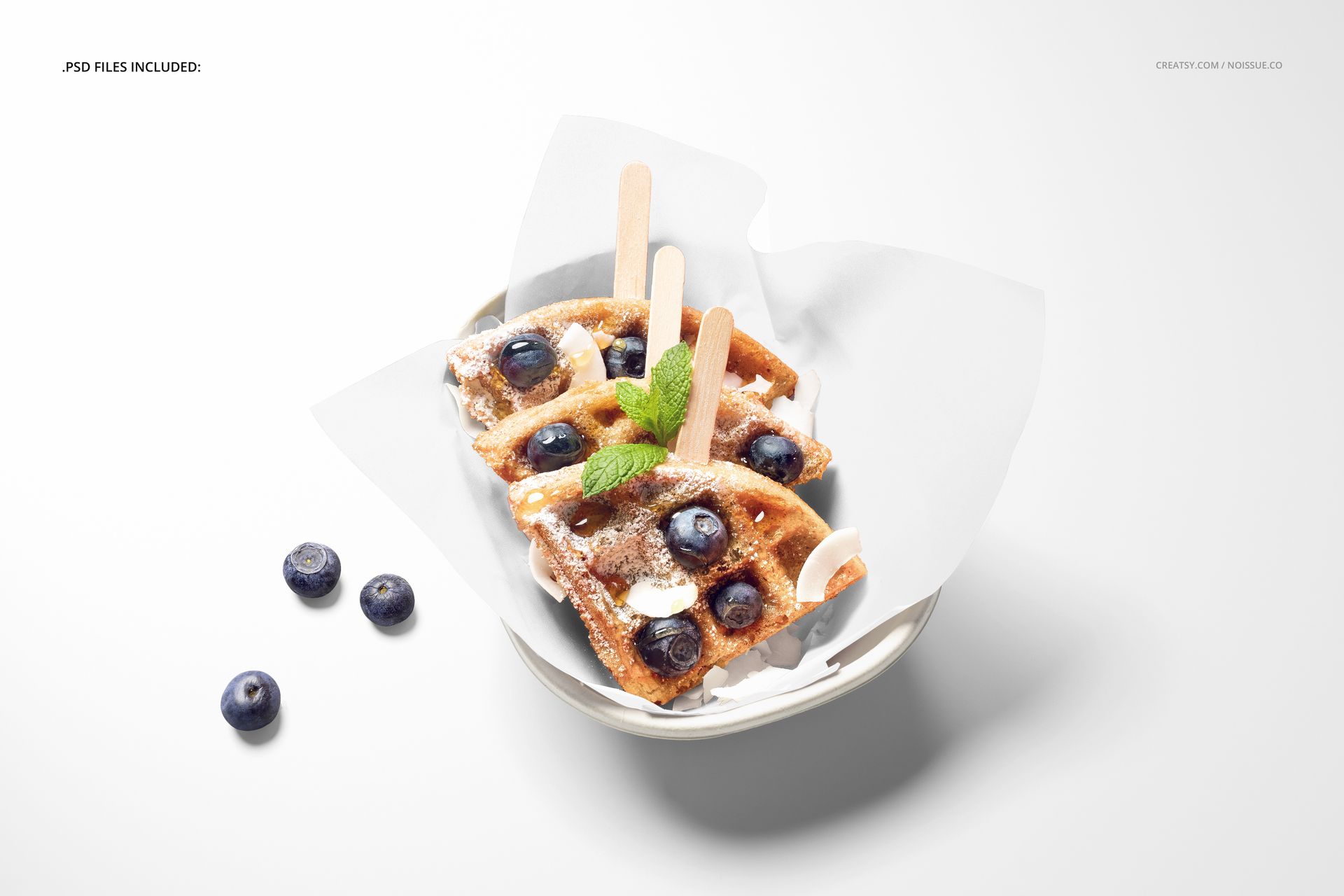PSD mockup featuring waffles on food safe paper, decorated with fresh blueberries, mint sprigs, and wooden sticks.