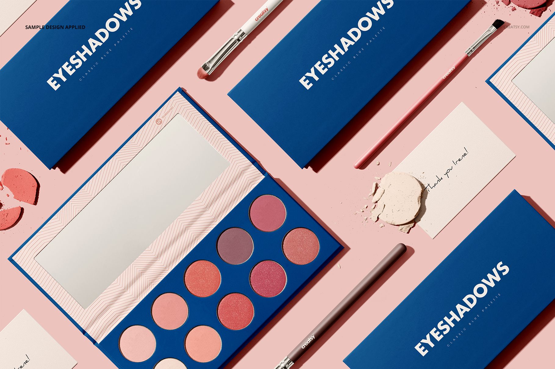 Eyeshadow palette mockup set with blue rectangular cases, round pans of pink and peach shades, and makeup brushes on a pink surface.