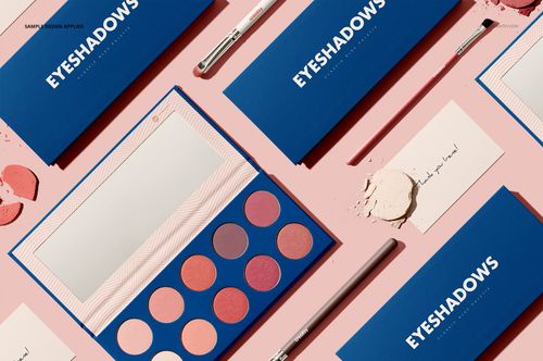 Eyeshadow palette mockup set with blue rectangular cases, round pans of pink and peach shades, and makeup brushes on a pink surface.