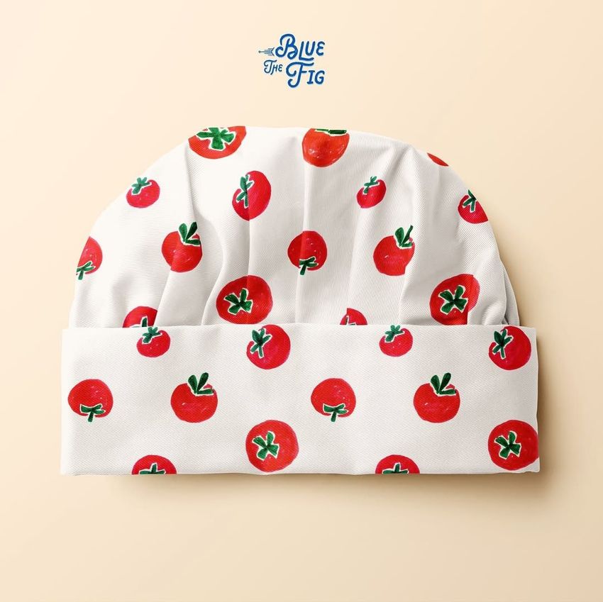 Kids apron mockup featuring a white chef hat with a playful red tomato pattern, displayed on a light beige background.