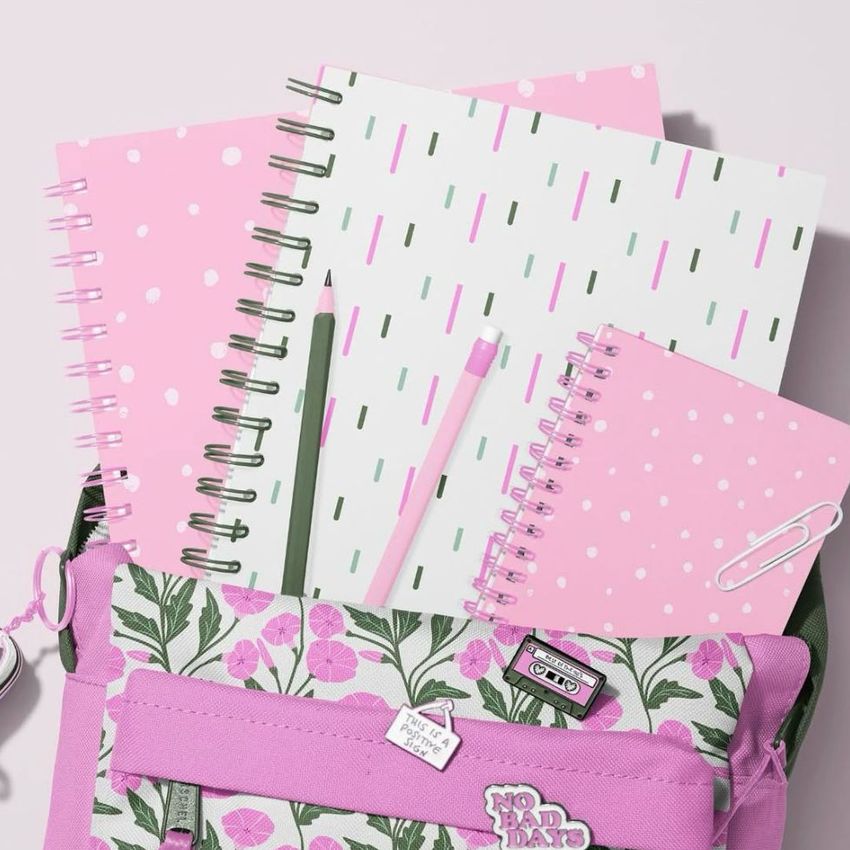 School backpack mockup with pink floral front pocket, holding spiral notebooks in pastel pink and white with dotted and striped patterns.