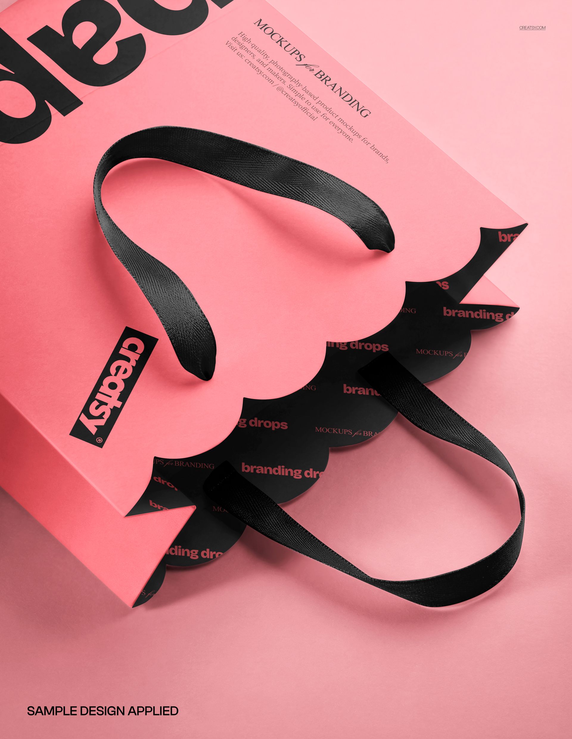 Front view of a scalloped paper bag mockup with black ribbon handles and bold branding on a pink background.