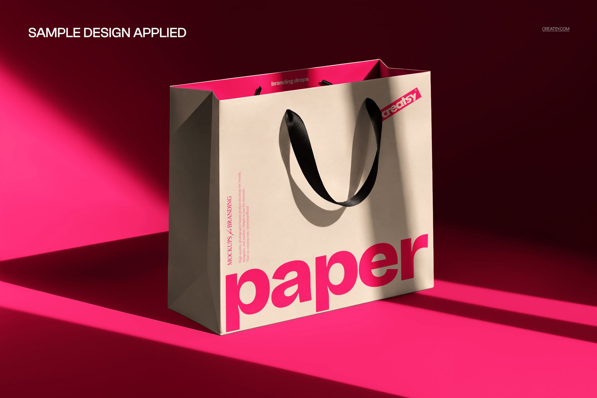 Premium paper bag mockup in sharp sunlight, beige with bold pink text, black handles, angled front view.