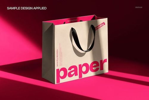 Premium paper bag mockup in sharp sunlight, beige with bold pink text, black handles, angled front view.