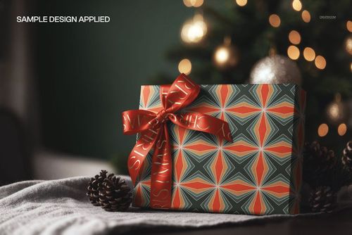 Front view of a Christmas gift box mockup featuring a bold geometric design, red ribbon, and festive background.