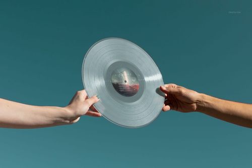 Clear colored vinyl record mockup displayed outdoors, with two hands holding the disc against a blue background.