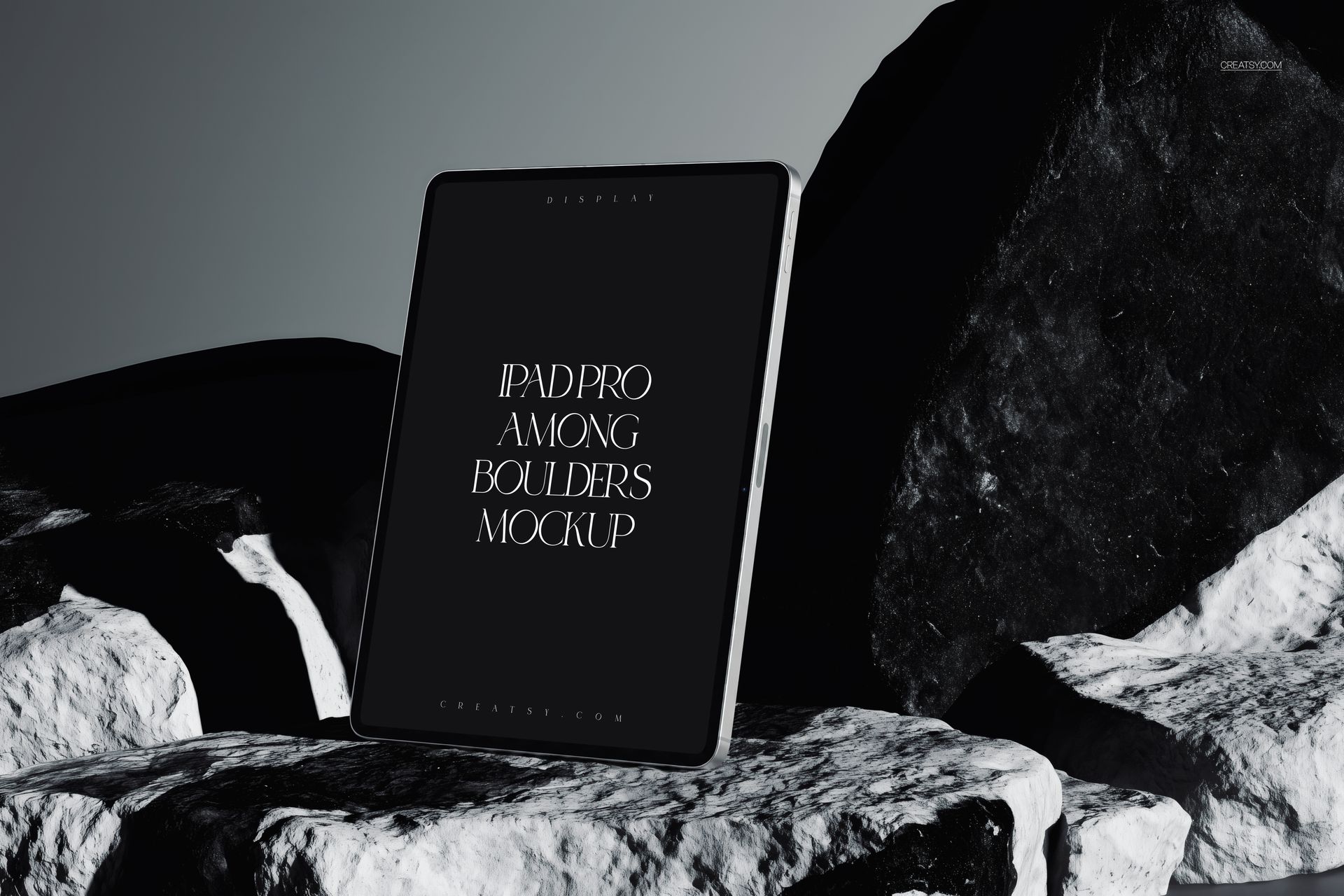 Front view of an iPad Pro mockup standing upright among large black and white boulders in a dramatic setting.