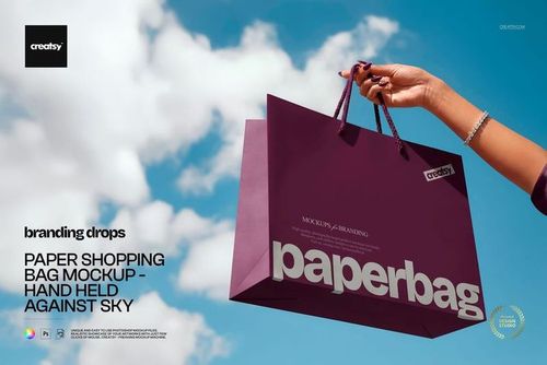 PSD mockup featuring a purple paper shopping bag held up outdoors, displaying modern typography and blue sky.