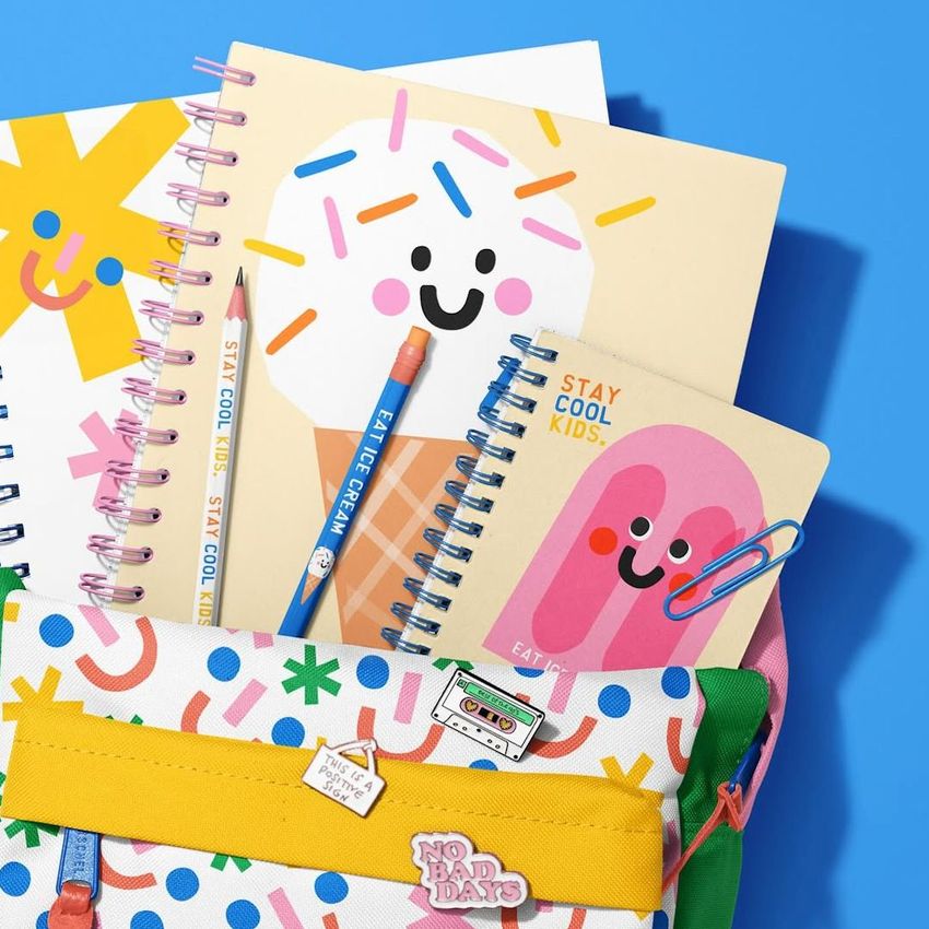 Colorful school backpack mockup with spiral notebooks featuring playful ice cream and popsicle illustrations on a blue background.