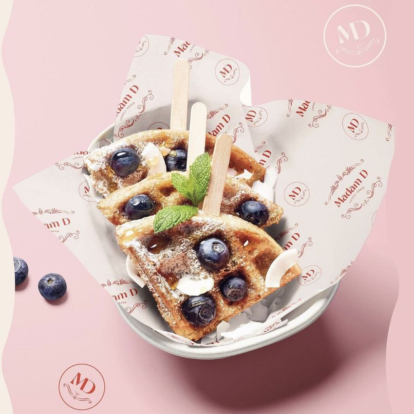 Food safe paper mockup showing a bowl with waffles topped with blueberries, coconut flakes, and mint, on branded wrapping paper.