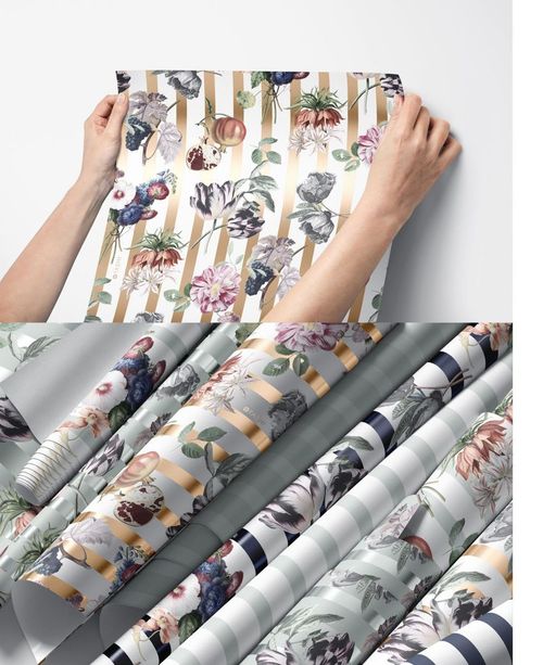 Person holding a decorative floral wallpaper sheet, with multiple rolled wallpaper mockups featuring stripes and flowers below.