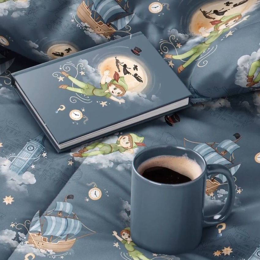 Microfiber comforter mockup featuring a playful children’s pattern with ships, clocks, and a character in green, shown with a matching book and blue mug.