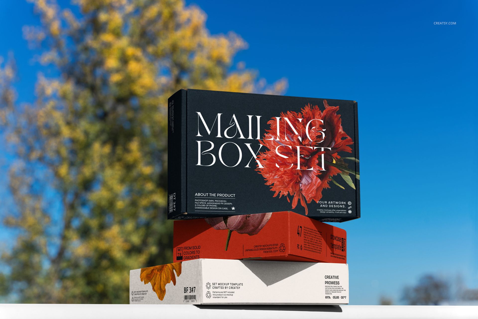 PSD mockup of three packaging boxes with flower graphics, photographed from the front in an outdoor setting.