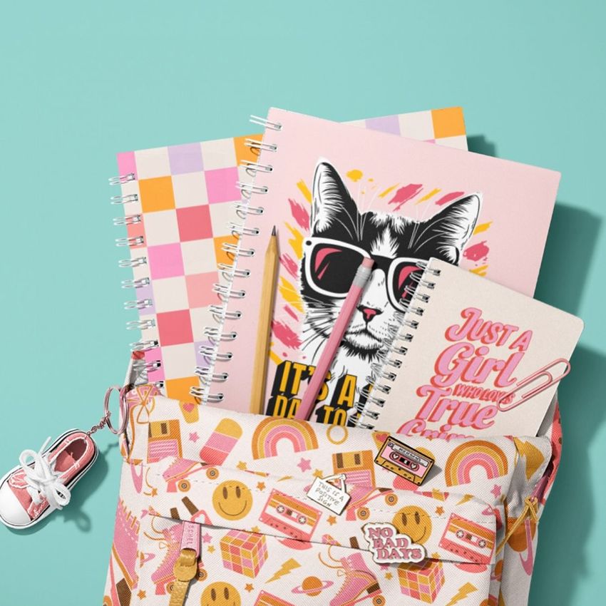 School backpack mockup with spiral notebooks featuring colorful covers, including a cat illustration and playful patterns on a teal background.