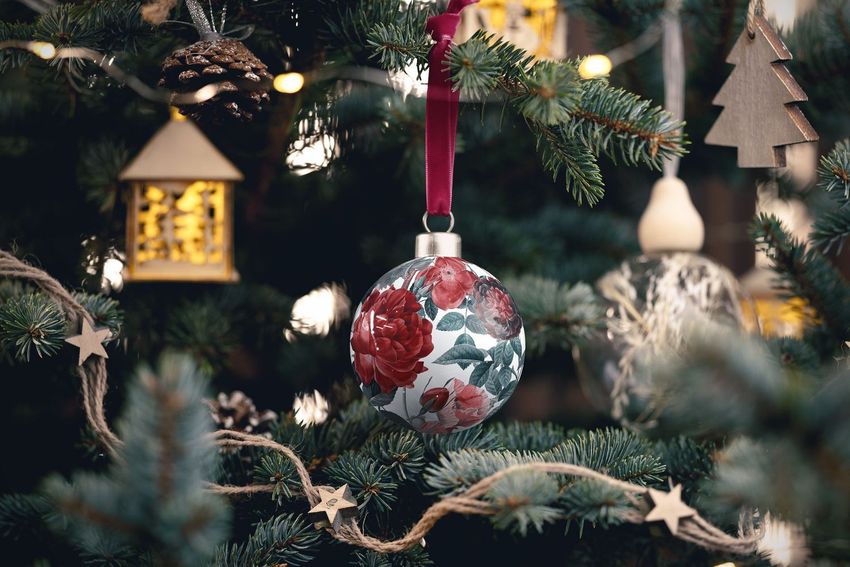 Handmade bone china Christmas bauble mockup with red rose pattern hanging on a decorated tree with lights and ornaments.